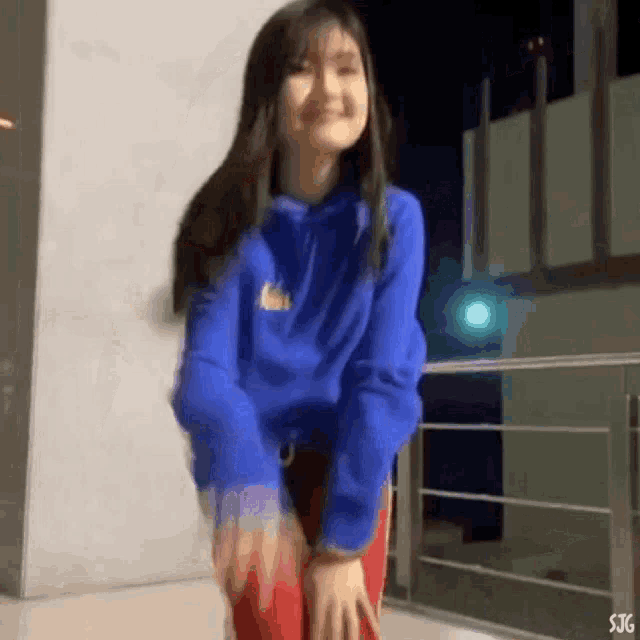 a girl in a blue hoodie and red pants is standing on a balcony .