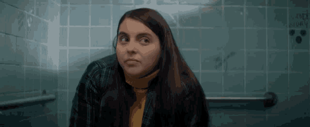 a woman in a yellow turtleneck is sitting in a bathroom next to a blue tiled wall .