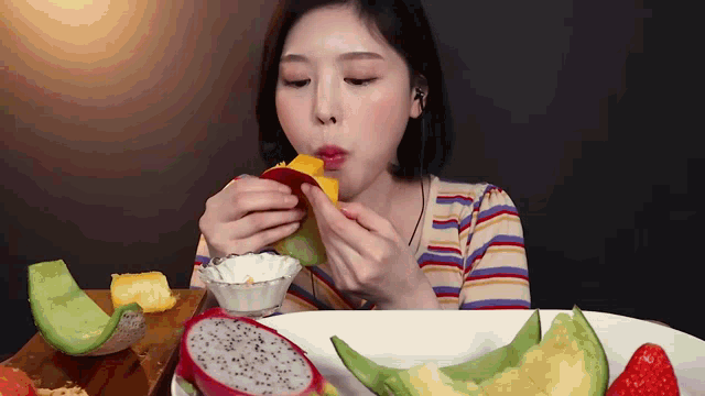 a woman is eating a slice of mango next to a plate of fruit