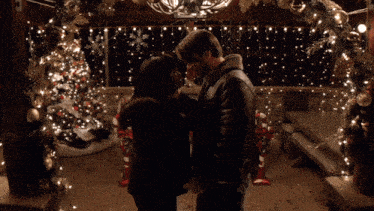 a man and woman are standing under a christmas wreath