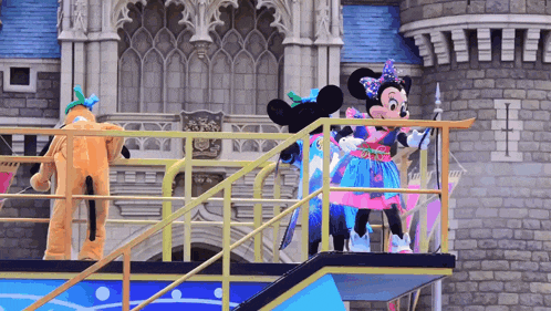 minnie mouse and pluto are dancing on a stage in front of a castle