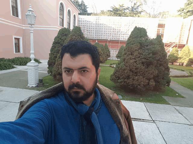 a man with a beard is taking a selfie in front of a building