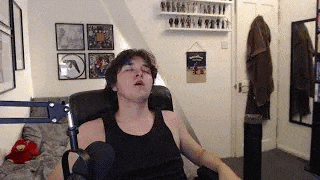 a man in a black tank top is sitting in a chair with his eyes closed in a room .