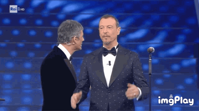 a man in a tuxedo stands next to another man in front of a microphone with the words rai hd on the bottom right