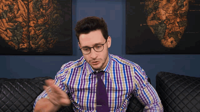 a man wearing glasses and a plaid shirt is sitting on a couch