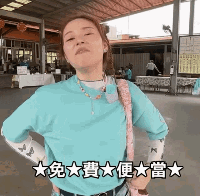 a woman in a blue shirt is standing with her hands on her hips in front of a building with chinese characters on it