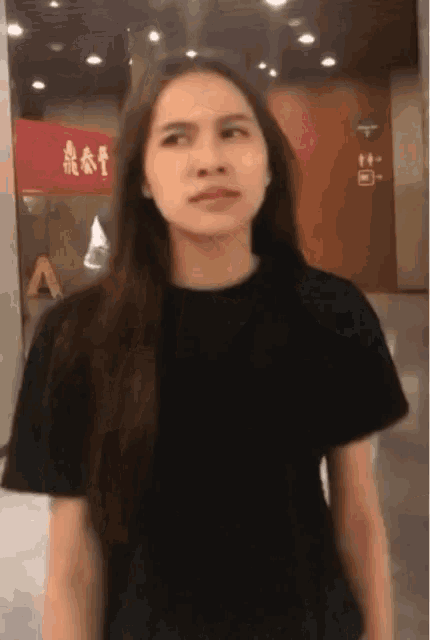 a woman with long hair wearing a black shirt is standing in front of a red sign that says a on it .