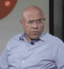 a bald man wearing glasses and a blue striped shirt is making a face .