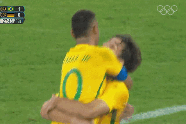 two soccer players hugging each other on a field with a scoreboard that says bra 1 ger 0