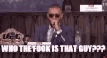 a man in a suit and tie is sitting at a table with a microphone in his mouth .