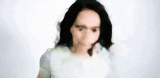 a young woman with long black hair is standing in front of a white background and her hair is blowing in the wind .