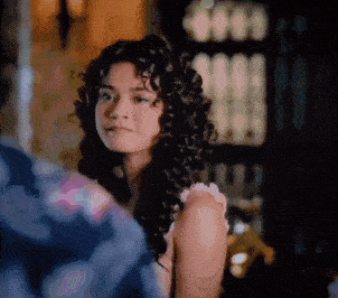 a woman with curly hair is looking at the camera in a room .