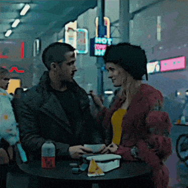a man and woman are sitting at a table in front of a sign that says hot dog hut