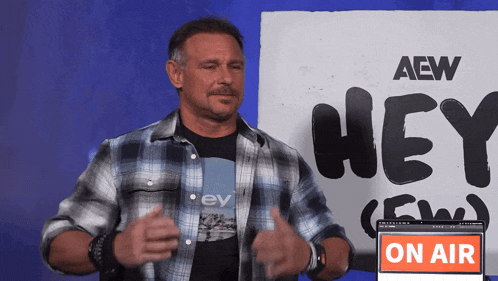 a man in a plaid shirt is standing in front of a sign that says hey