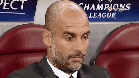a bald man with a beard sits in front of a champions league sign