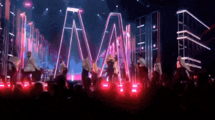 a group of people are dancing on a stage with a large m in the background