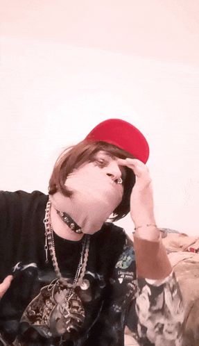 a person wearing a red hat and a black shirt with a skull on it is covering their face with their hand