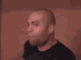 a bald man with a beard is making a funny face and pointing at the camera with his mouth open .