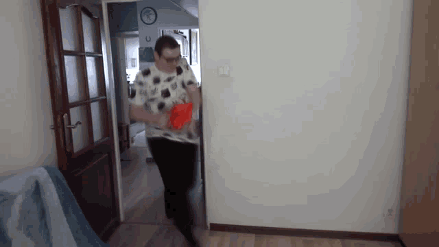 a man in a polka dot shirt is running through a hallway holding a red object