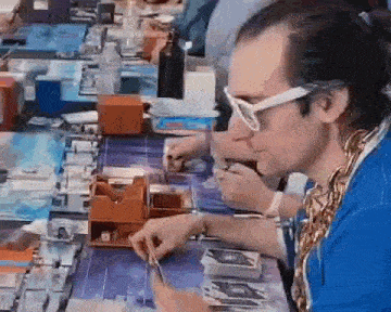 a man wearing sunglasses and a blue shirt is sitting at a table playing a game of cards .