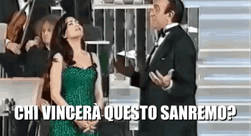 a woman in a green dress is standing next to a man in a tuxedo and talking to him .