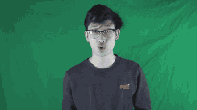 a man wearing glasses and a black shirt is standing in front of a green wall .