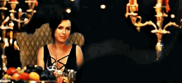 a woman in a black dress is sitting at a table with candles .