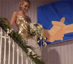 a woman in a gold dress is holding a bouquet of flowers while standing on a set of stairs