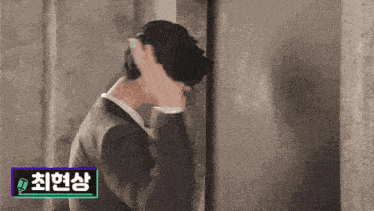 a man in a suit is leaning against a wall with a sticker that says ' 최현상 ' on it