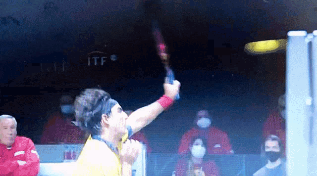 a man in a yellow shirt is holding a tennis racket in front of a sign that says itf