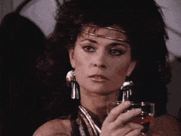 a woman is holding a glass of wine in her hand and looking at the camera .