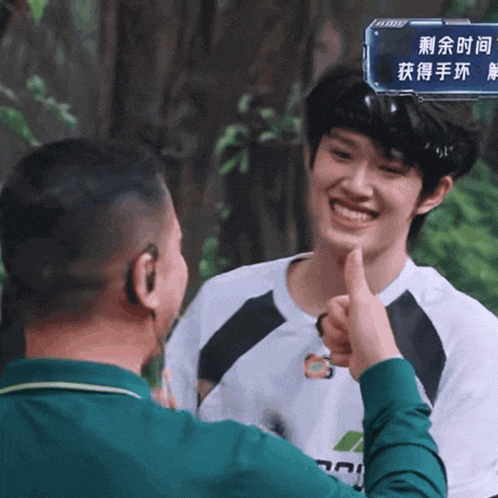 a man giving a thumbs up to another man with chinese writing on the screen behind him
