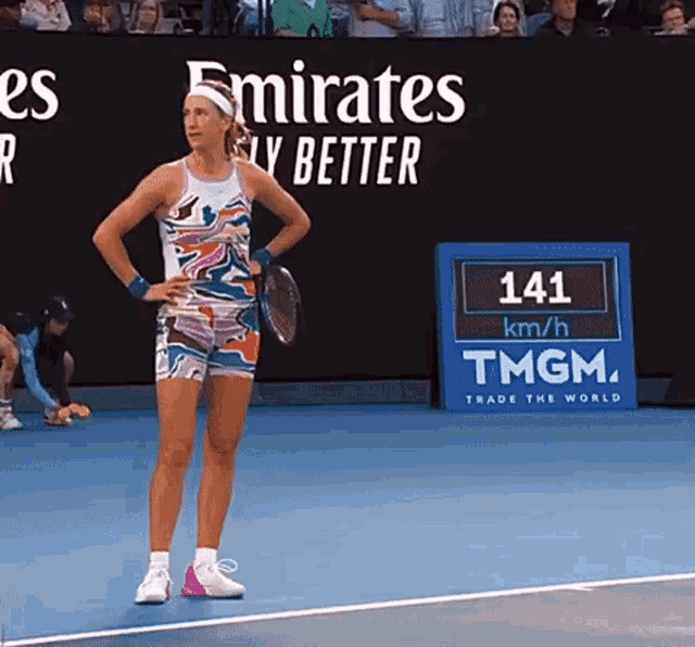 a woman holding a tennis racquet on a tennis court in front of an emirates fly better sign
