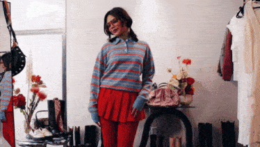 a woman wearing a blue and red striped sweater and a red pleated skirt is standing in front of a mirror