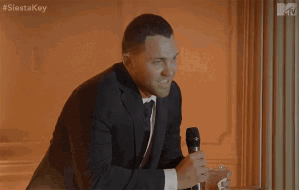 a man in a suit and tie holds a microphone and says cheers to that