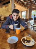 a young man is sitting at a table in a restaurant holding two cups of coffee