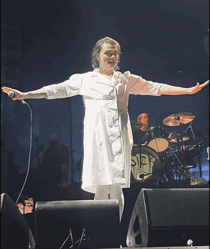 a woman in a white dress stands in front of a drum set that says sick on it