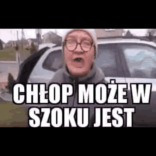 a man wearing glasses and a beanie is standing in front of a car and yelling .