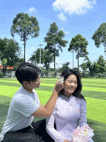 a man putting flowers on a woman 's ear while she holds a bouquet