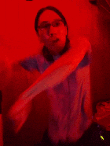 a woman wearing glasses is standing in front of a red light and making a fist .