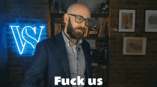 a man with glasses says fuck us in front of a brick wall