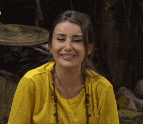 a woman wearing a yellow shirt and a necklace smiles for the camera