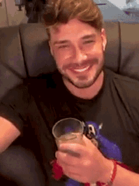 a man with a beard is sitting on a couch holding a glass of beer .