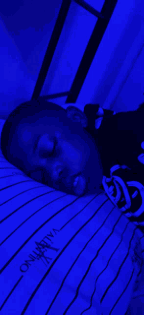 a young boy is sleeping on a bed with a blue valentino pillow