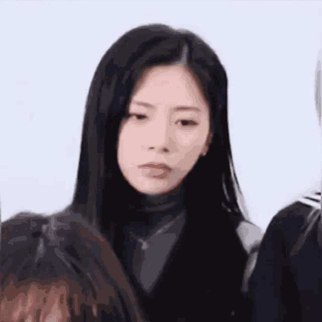a woman with long black hair is standing next to a group of people and making a funny face .