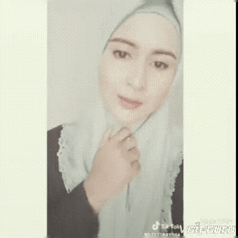 a woman wearing a hijab and a white scarf is looking at the camera while holding a pen in her hand .
