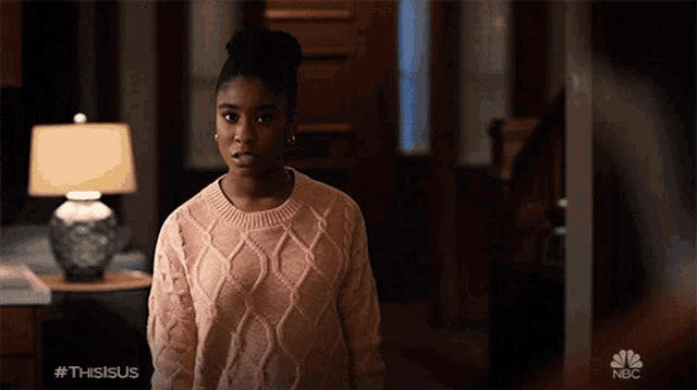 a woman in a pink sweater is standing in a room with a nbc logo behind her