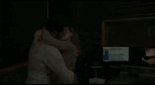 a man and a woman kiss in front of a computer monitor