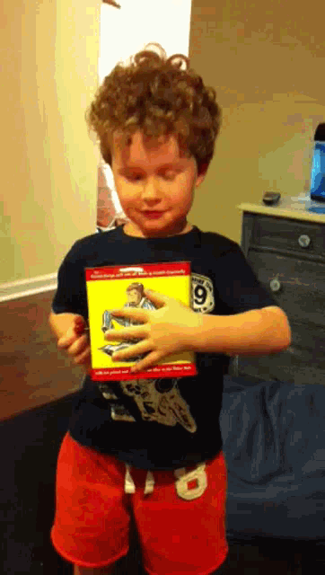 a young boy wearing a black shirt with the number 9 on it holds a yellow box