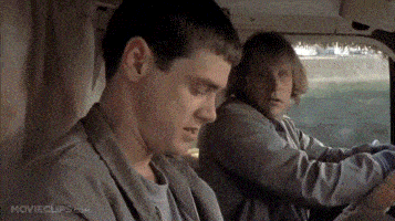 a man is sitting in the back seat of a car while another man drives .